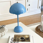 Load image into Gallery viewer, A blue rechargeable LED small desk lamp is placed on a coffee table next to a book titled &quot;Kaffe Koebenhavn&quot; and a woven basket. The lamp features a modern and minimalist design, providing a playful yet sophisticated look to the space with the light wooden floor and simple white surroundings.
