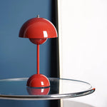 Load image into Gallery viewer, A vibrant red rechargeable LED small desk lamp sits elegantly on a glass table. The background features a contrasting blue wall, creating a striking color combination that highlights the modern design of the lamp.
