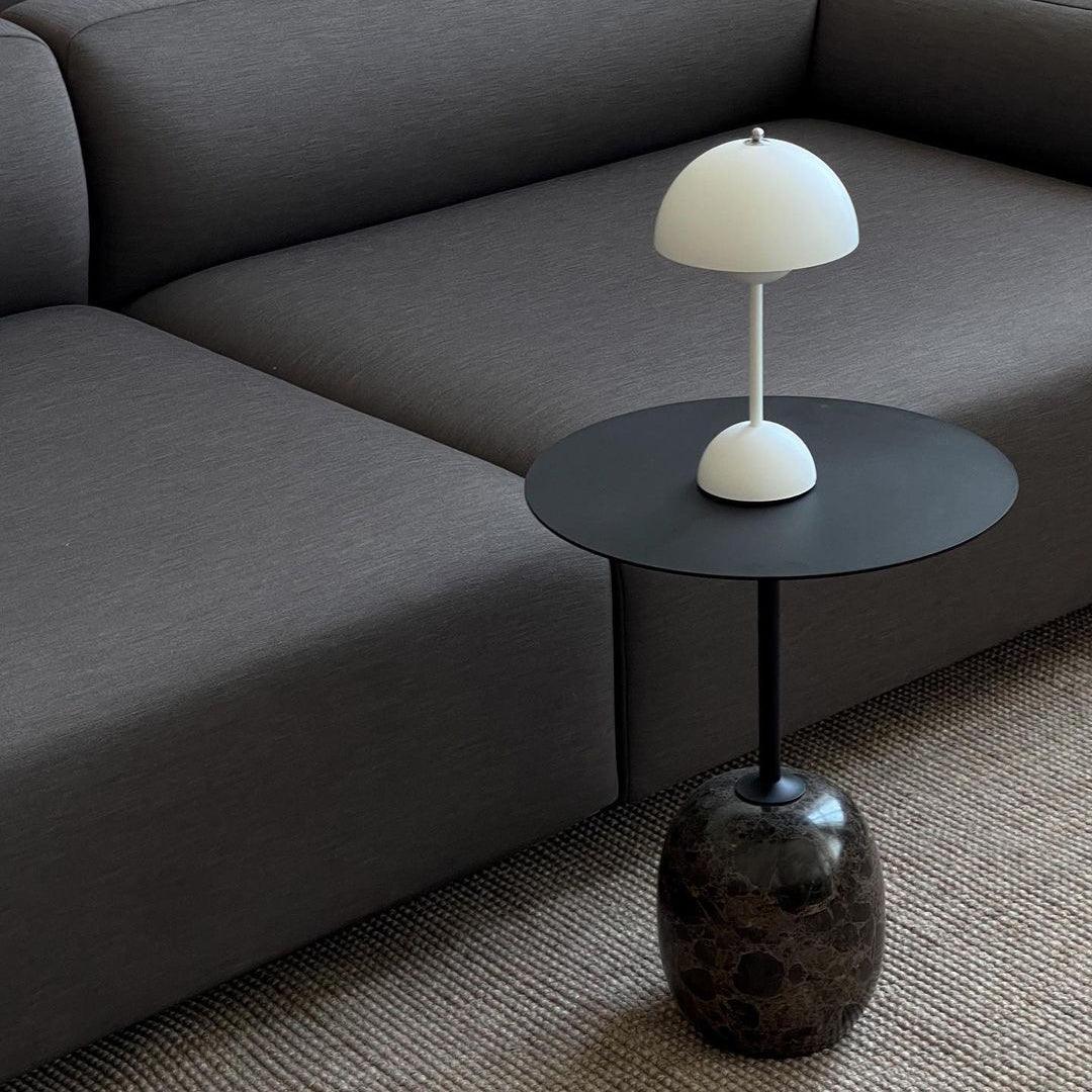 A white rechargeable LED small desk lamp stands on a minimalist black side table with a marble base, placed next to a dark gray sofa. The clean, modern aesthetic creates a stylish and serene atmosphere in the living room.