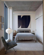 Load image into Gallery viewer, In this serene bedroom setting, a rice paper floor lamp provides soft, ambient lighting, complementing the clean, modern decor. The warm glow of the lamp contrasts with the cool tones of the concrete ceiling and the minimalist artwork above the bed. The calming color palette of the room, paired with the soft texture of the bed linens and chair, creates a peaceful retreat.
