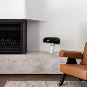 A contemporary interior featuring the Snoopy Table Lamp with a black dome shade and marble base placed on a stone fireplace ledge, alongside a tan leather armchair and minimalist decor.