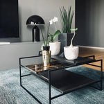 Load image into Gallery viewer, Atollo Metal Table Lamp in black, showcased on a side table in a contemporary living room setting, accompanied by decorative plants and a sleek coffee table on a textured blue rug, reflecting an elegant and modern home decor style.
