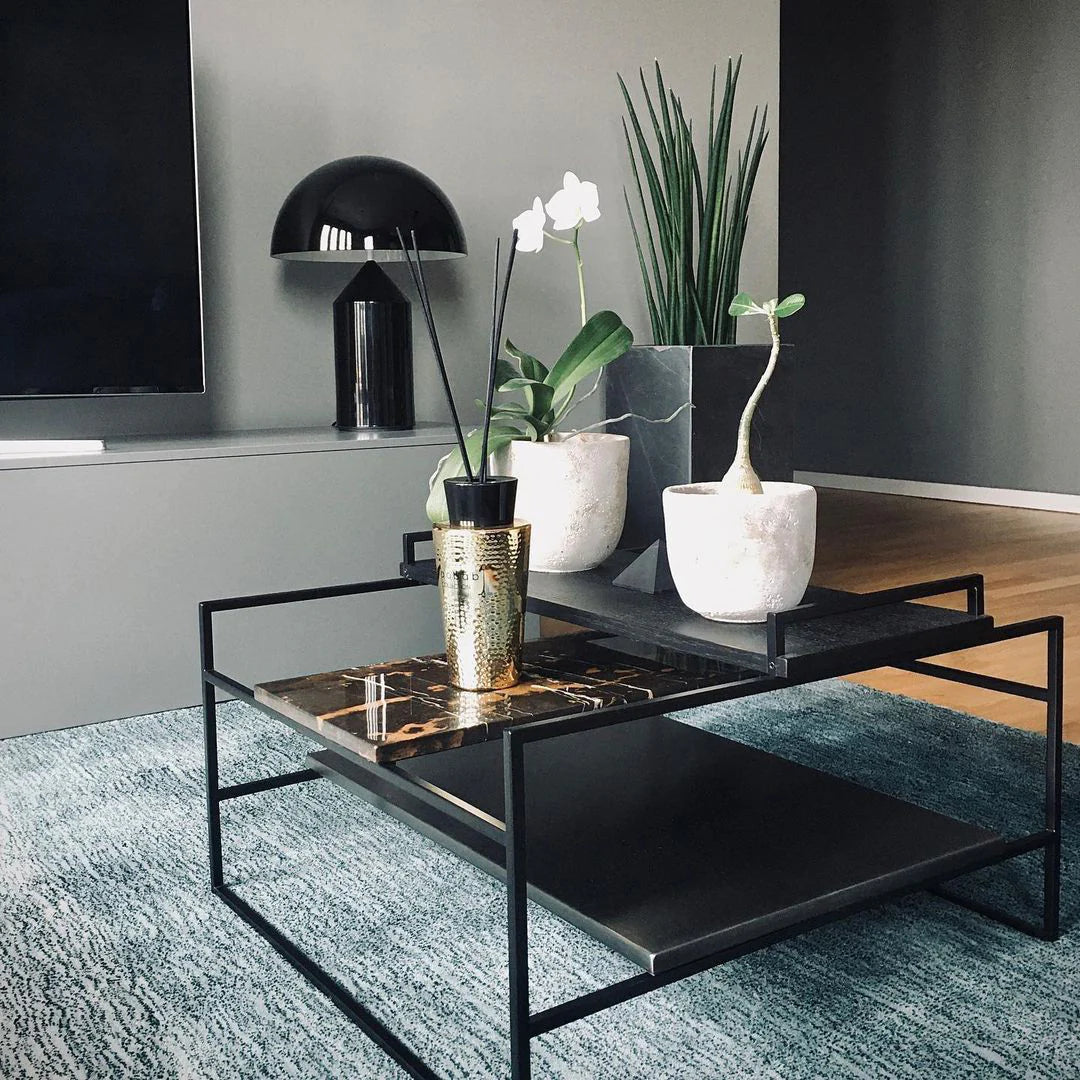 Atollo Metal Table Lamp in black, showcased on a side table in a contemporary living room setting, accompanied by decorative plants and a sleek coffee table on a textured blue rug, reflecting an elegant and modern home decor style.