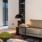 Load image into Gallery viewer, Atollo Metal Table Lamp in black, placed beside a chic beige sofa in a spacious, minimalist living area with a large window, bookshelf, and sleek furnishings, creating a sophisticated and welcoming atmosphere.
