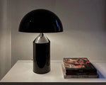 Load image into Gallery viewer, Atollo Metal Table Lamp in black featured on a sleek shelf alongside a stack of art books, highlighting a minimalist and cultured home decor style.
