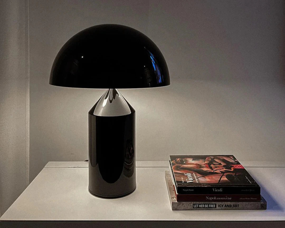 Atollo Metal Table Lamp in black featured on a sleek shelf alongside a stack of art books, highlighting a minimalist and cultured home decor style.