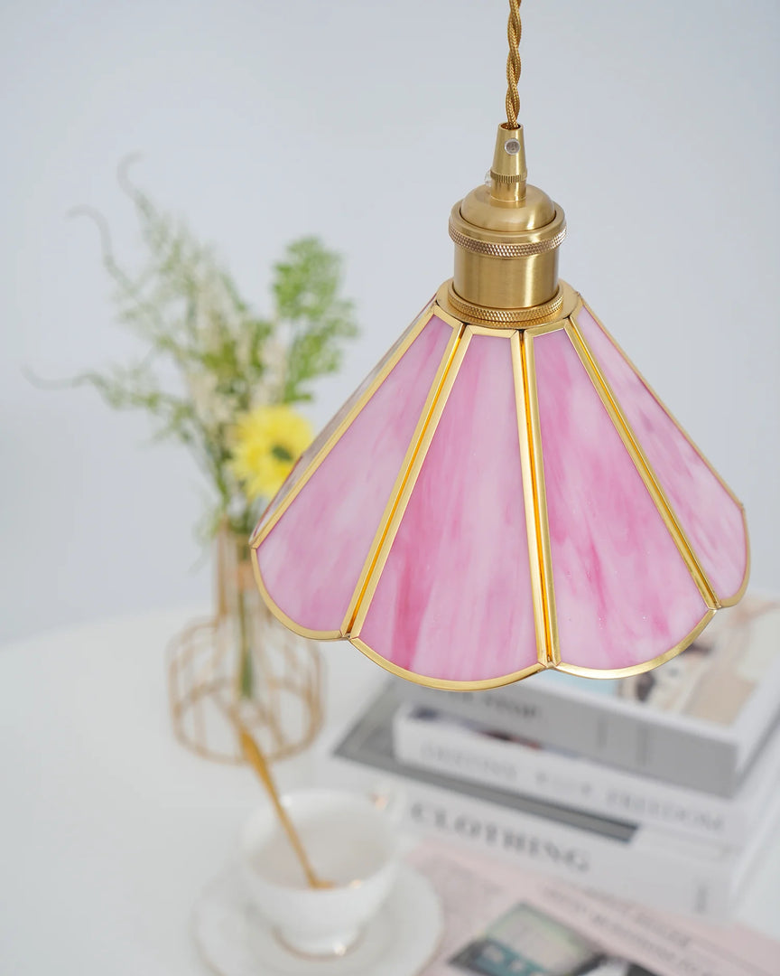 Close-up of the Butterfly pendant lamp with a pink stained glass scalloped shade and gold metal accents, hanging above a white table set with books, a teacup, and a floral arrangement in the background, showcasing its elegant craftsmanship.