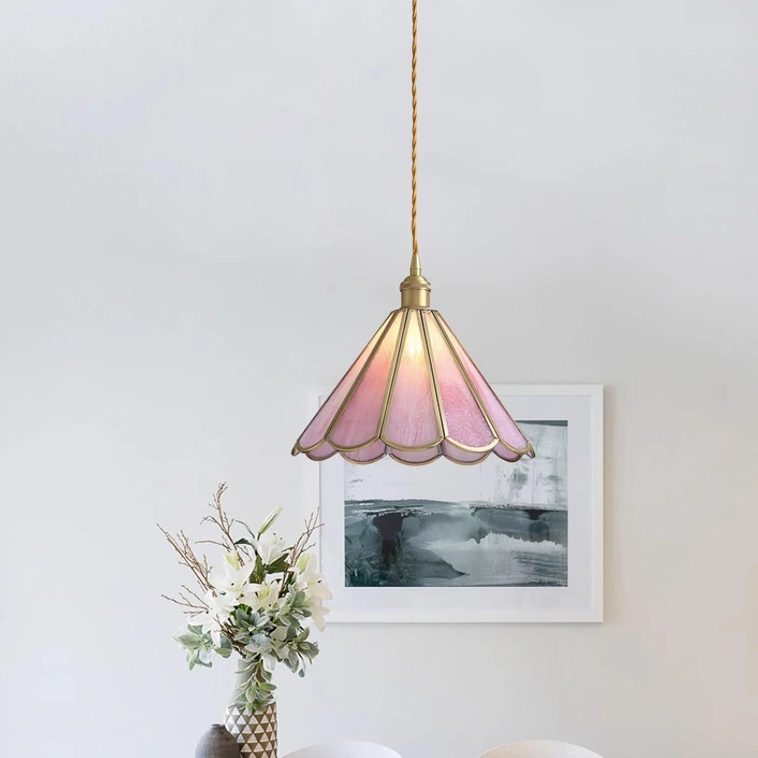 Butterfly pendant lamp with a pink stained glass scalloped shade and gold accents, hanging in a dining room with a minimalist white wall, abstract artwork, and a floral arrangement in a patterned vase, creating a chic and inviting ambiance.