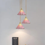 Load image into Gallery viewer, Trio of Butterfly pendant lamps with pink stained glass scalloped shades and gold accents, elegantly suspended at different heights on twisted cords, illuminating a wall with soft, warm light in a contemporary setting.
