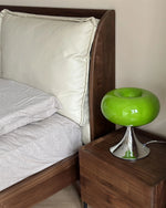 Load image into Gallery viewer, Candle table lamp with a glossy green glass dome-shaped shade and polished chrome base, placed on a wooden bedside table next to a modern bed with neutral bedding and a padded headboard, adding a sleek and stylish touch to the bedroom decor.
