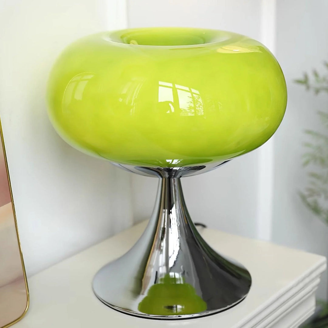 Candle table lamp featuring a bright green glass dome-shaped shade and a sleek polished chrome base, displayed on a white surface with a mirror edge and soft greenery in the background for a fresh, modern aesthetic.