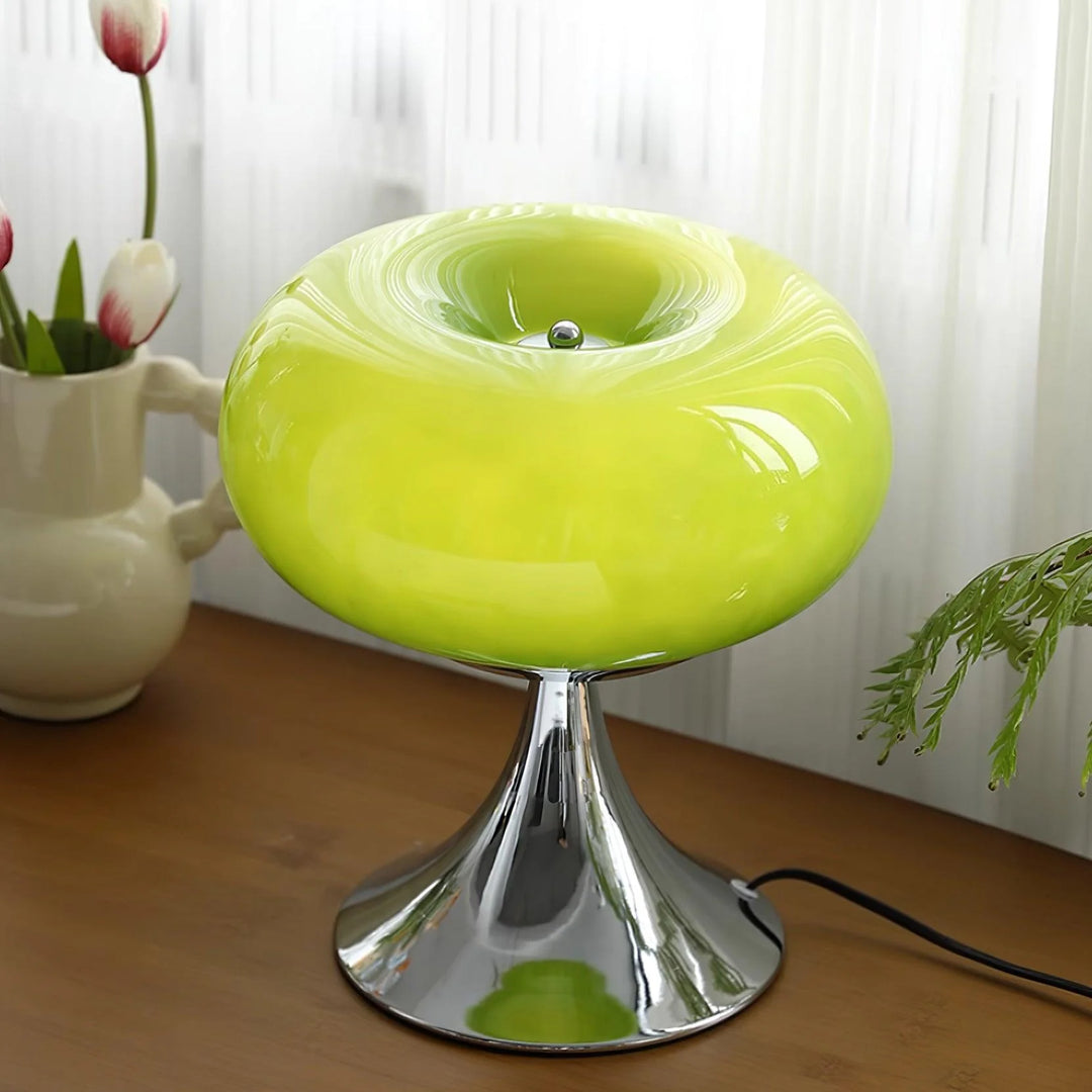 Candle table lamp with a vibrant green glass dome-shaped shade and polished chrome base, placed on a wooden surface with tulips in a ceramic vase and greenery in the background, creating a fresh and natural decor vibe.