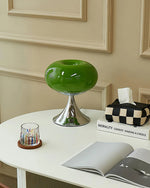 Load image into Gallery viewer, Candle table lamp with a glossy green glass dome-shaped shade and polished chrome base, styled on a white desk with an open magazine, a colorful glass candle holder, and a checkered tissue box, creating a modern and eclectic study space.
