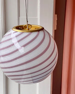 Load image into Gallery viewer, Candy pendant lamp with soft pink and white spiral design. The gentle pink and white swirls evoke a sense of calm and coziness in a chic, minimalist room with light neutral walls and soft fabrics. The lamp hangs elegantly by a brass fixture, casting a warm glow over a peaceful space adorned with pastel curtains, contributing to a serene and welcoming atmosphere.
