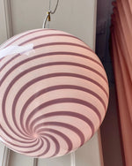 Load image into Gallery viewer, Candy pendant lamp with soft pink and white swirl design. The lamp adds a delicate touch to a serene room, where soft sunlight pours in through large windows, highlighting the swirling pattern. The soft pink tones blend beautifully with the neutral-colored walls, enhancing the overall peaceful atmosphere of the space.
