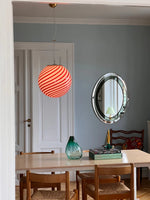 Load image into Gallery viewer, This red and white striped Candy pendant lamp suspended from the ceiling adds a playful touch, complementing a modern and stylish dining space with wooden chairs and a decorative vase.
