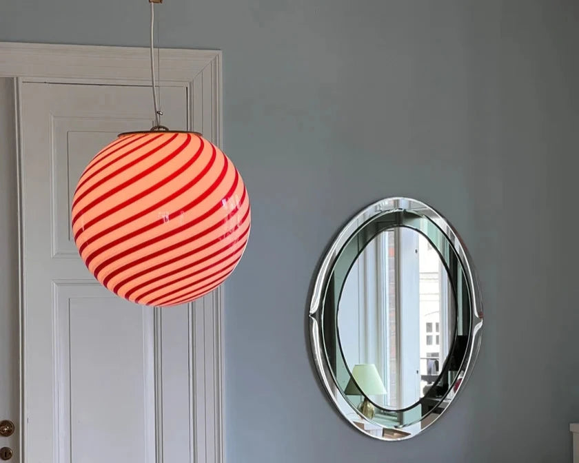 Candy pendant lamp with a vibrant red and white striped globe-shaped shade, suspended in front of a large oval mirror, adding a playful and bold touch to the modern room decor.