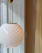 Load image into Gallery viewer, Candy pendant lamp with elegant white spiral design. The soft, white swirls create a serene and calming effect in a minimalist room with warm neutral-toned walls. Large windows allow natural light to illuminate the room, highlighting the gentle curves of the lamp and giving the space an inviting and tranquil atmosphere.
