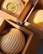 Load image into Gallery viewer, Candy pendant lamp with yellow and white swirl pattern, carefully packed in boxes, showcasing its striking design. The lamp is placed in cardboard packaging, with a hint of brass details peeking through the boxes. The image captures a bright, well-lit room, with sunlight reflecting off the lamp’s glossy surface, adding warmth and charm.
