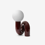 Load image into Gallery viewer, A studio shot of the Caterpillar Table Lamp featuring a glossy burgundy curved base and a smooth white globe light, displayed against a clean white background to highlight its sculptural and contemporary design.
