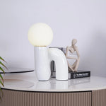 Load image into Gallery viewer, A Caterpillar Table Lamp with a glossy white curved base and soft glowing globe light placed on a modern ribbed beige console table, styled alongside minimalist decor pieces, including a neutral abstract sculpture and stacked design books, in a contemporary living space.
