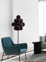 Load image into Gallery viewer, The Cépage Floor Lamp with deep burgundy globe-shaped lights on a black stand, styled in a modern lounge area featuring a teal mid-century armchair, a black side table, a gray sofa, and a textured area rug, creating a sleek and contemporary space.
