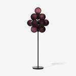 Load image into Gallery viewer, A studio shot of the Cépage Floor Lamp featuring a sleek black stand and base with an elegant arrangement of burgundy ribbed glass globes, displayed against a clean white background to highlight its modern and sculptural design.
