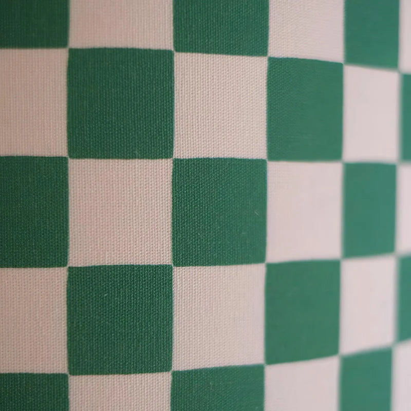 A close-up view of a bold green and white checker pattern, showcasing the texture and weave of the fabric. The crisp, contrasting squares create a dynamic visual effect, highlighting the classic yet playful design perfect for modern decor elements such as lampshades or upholstery.