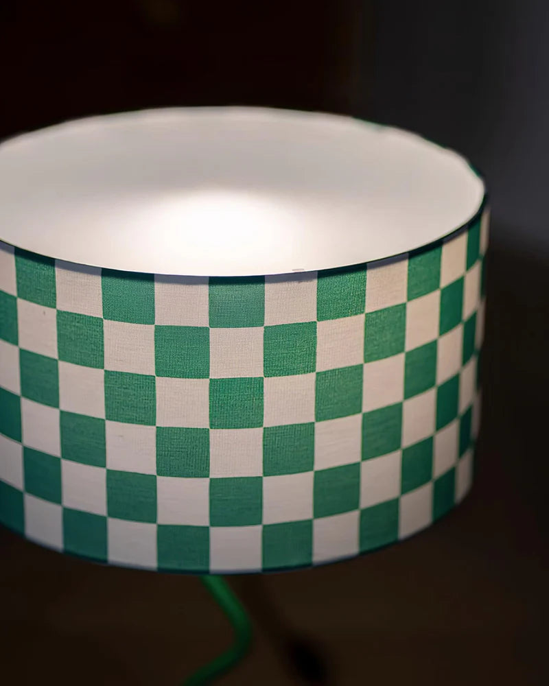 A close-up of a green and white checkerboard-patterned lampshade, capturing the fabric's fine texture and the soft glow emanating from within. The rounded edge and inner white lining create a balanced contrast, emphasizing the modern and playful design of this statement decor piece.