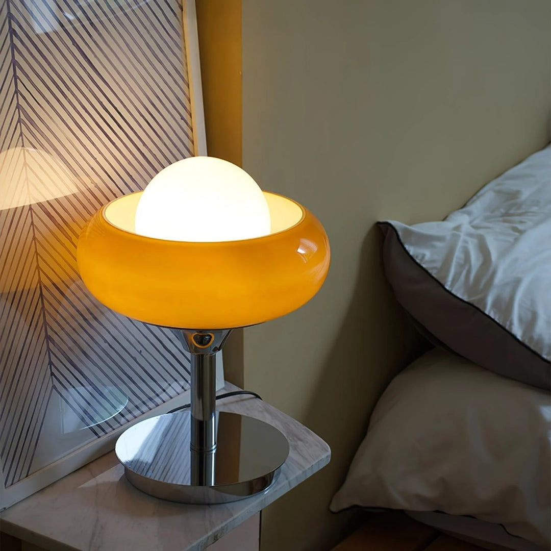 Crostata Table Lamp placed on a marble nightstand, featuring a glowing orb encased in an orange glass bowl, creating a cozy and ambient lighting effect in a modern bedroom setting.