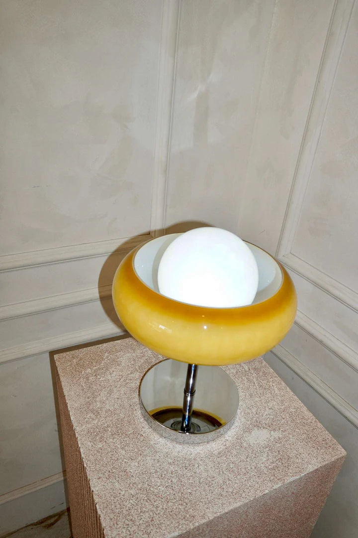 Top view of the Crostata Table Lamp showcasing its spherical glowing orb nestled within a bold orange glass bowl, positioned on a textured pedestal against a neutral-toned wall.