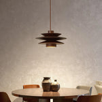 Load image into Gallery viewer, Cylindrical Pendant Light with a layered metal design, suspended over a round dining table adorned with decorative vases, casting a warm ambient glow in an elegant, textured dining space.
