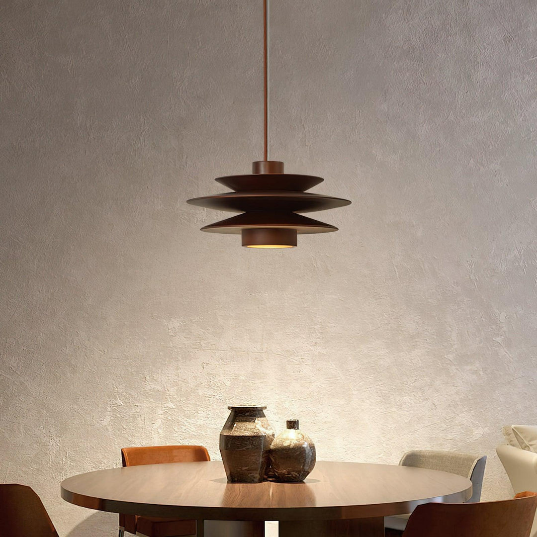 Cylindrical Pendant Light with a layered metal design, suspended over a round dining table adorned with decorative vases, casting a warm ambient glow in an elegant, textured dining space.