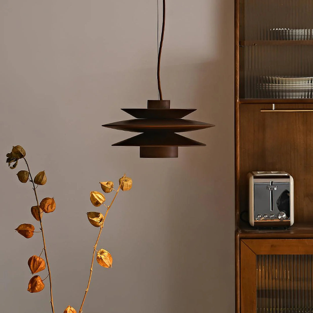 Cylindrical Pendant Light with a tiered metal design in a deep brown finish, suspended in a minimalist kitchen setting with wooden cabinetry and dried botanical decor, creating a warm and inviting ambiance.