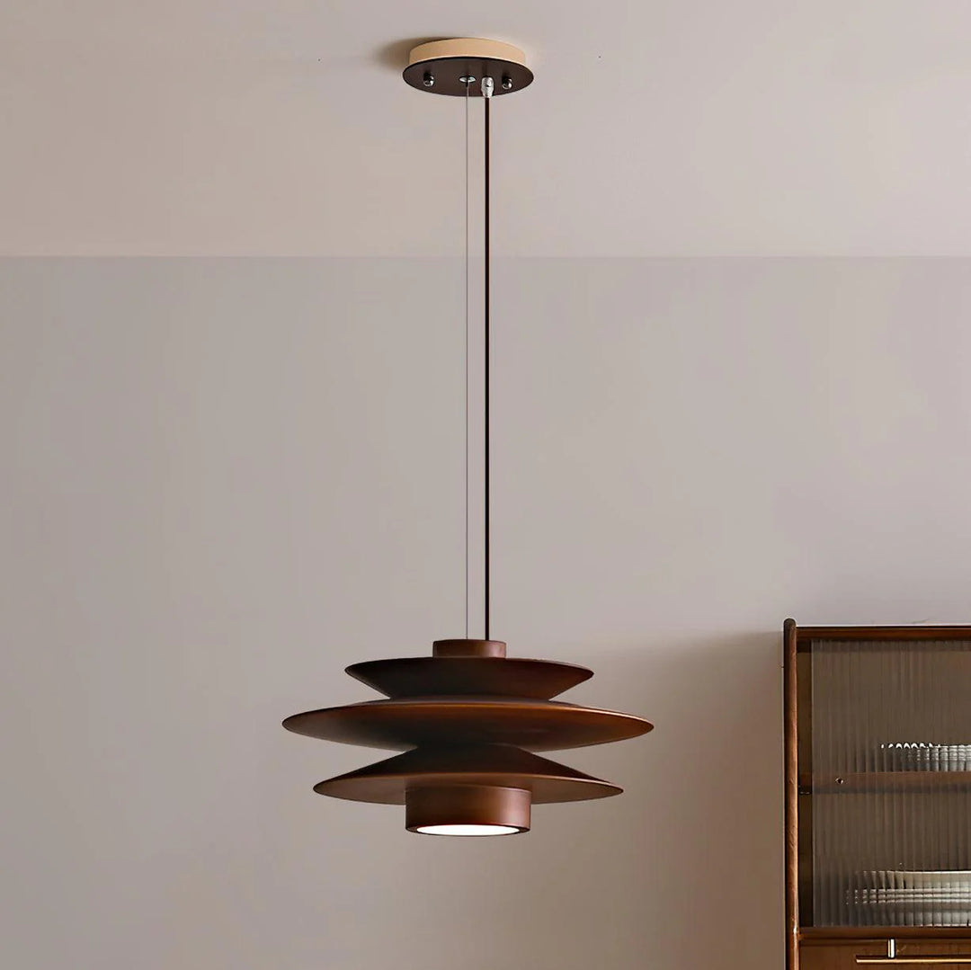 Cylindrical Pendant Light with a layered design in a warm brown finish, suspended from the ceiling in a contemporary room, complementing minimalist decor with soft lighting and wooden furniture accents.