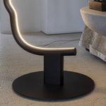 Load image into Gallery viewer, Close-up view of the face-shaped lamp’s black circular base and curved illuminated design, resting on a textured floor next to a round modern table.
