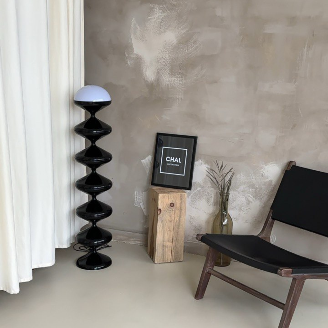 Modern interior featuring the Gourd Floor Lamp with a unique stacked black gourd design and white dome, set in a minimalist room with a distressed grey wall, wooden stump side table, and a sleek black chair.