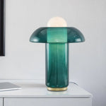 Load image into Gallery viewer, Elegant green glass table lamp with a rounded dome top and gradient glass base featuring a gold accent, placed on a sleek white tabletop in a minimalist room setting.
