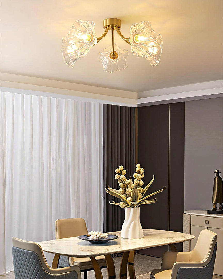 A sophisticated dining room illuminated by the Kalin Flower Glass Ceiling Light, featuring a brushed gold frame and delicate petal-shaped glass shades. The ceiling light's warm glow enhances the luxurious ambiance of the room, highlighting the elegant marble dining table, quilted chairs, and a striking centerpiece of dried flowers in a white ceramic vase. The floor-to-ceiling drapery adds a soft, refined touch to the modern decor.