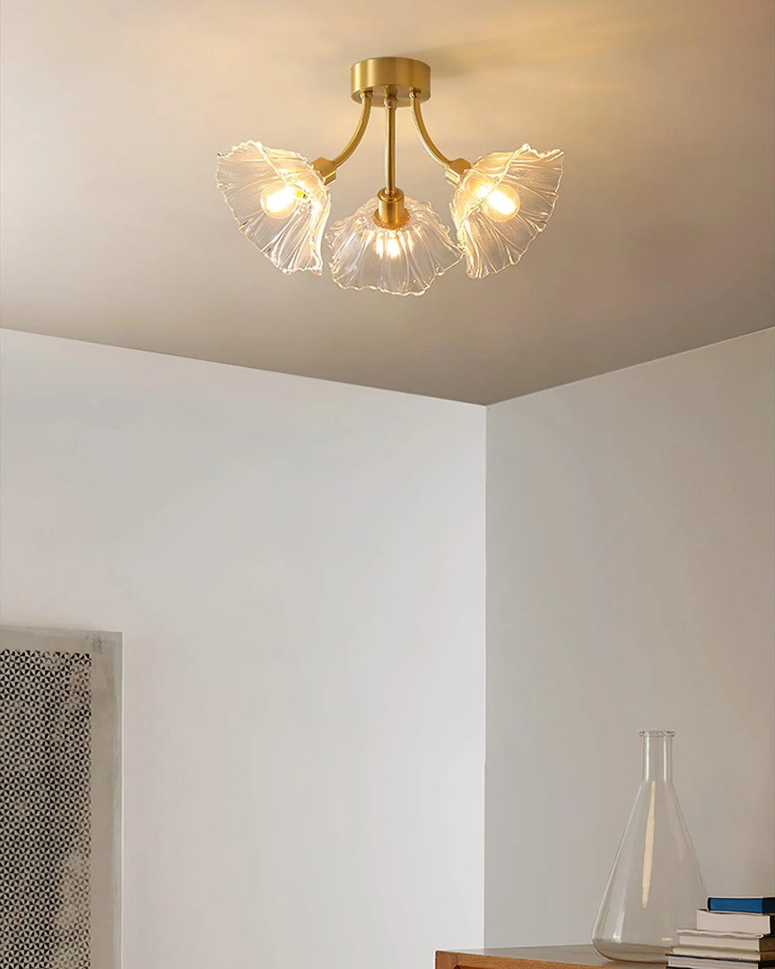 A minimalist room featuring the Kalin Flower Glass Ceiling Light with its elegant gold fixture and three petal-shaped glass shades. The ceiling light's soft glow enhances the clean, neutral-toned space, while simple decor elements, such as a glass vase and neatly stacked books, contribute to the serene and modern aesthetic.