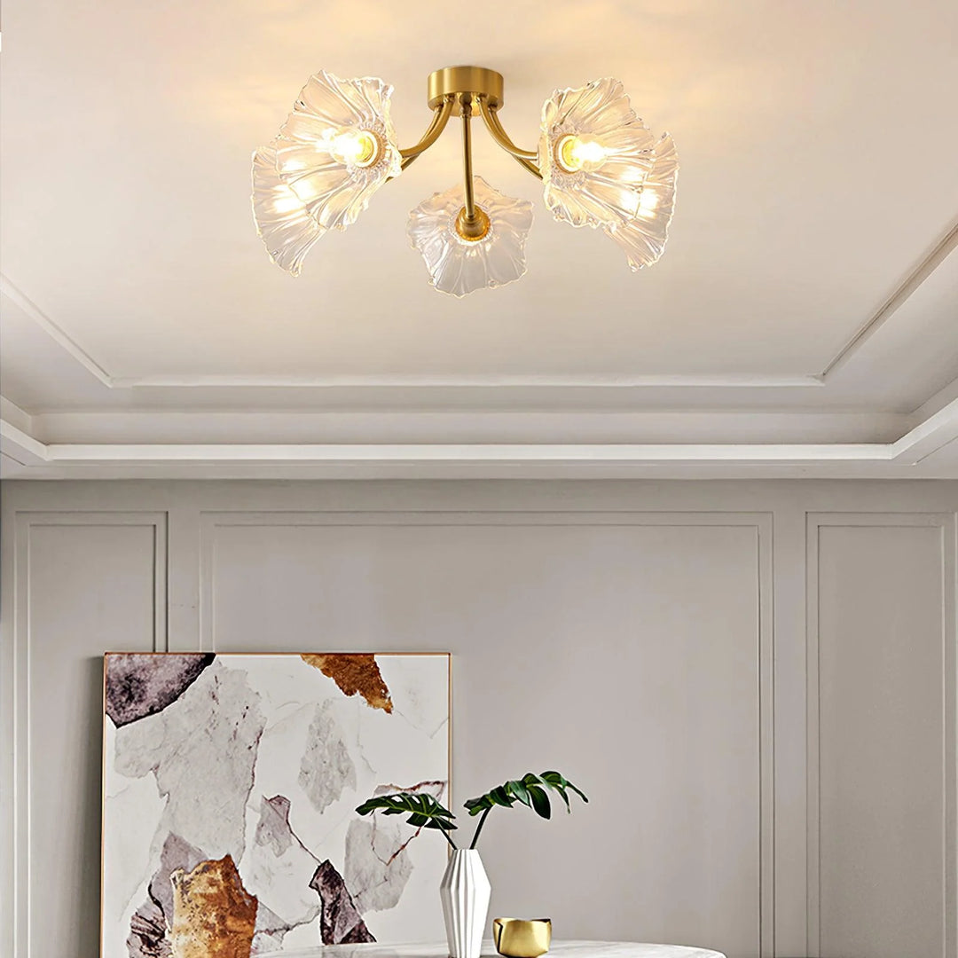 A modern room setting showcasing the Kalin Flower Glass Ceiling Light with its elegant gold fixture and petal-shaped glass shades. The ceiling light casts a warm and inviting glow, complementing the neutral-toned room decor, which includes a contemporary abstract painting, a sleek white vase, and a green leafy accent, creating a refined yet cozy ambiance.