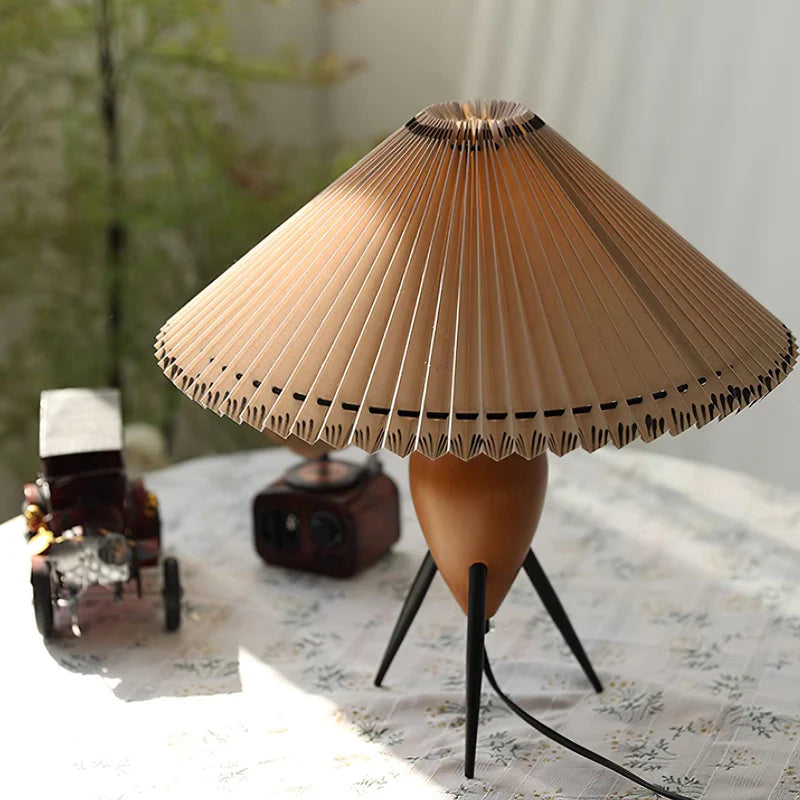 The Makie Table Lamp placed on a patterned tablecloth beside decorative items, including a miniature vintage car and retro speaker, bathed in natural sunlight for a cozy ambiance.