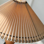 Load image into Gallery viewer, Close-up of the Makie Table Lamp&#39;s pleated fabric shade, showing intricate folds and a decorative stitched edge with a warm light glowing through.
