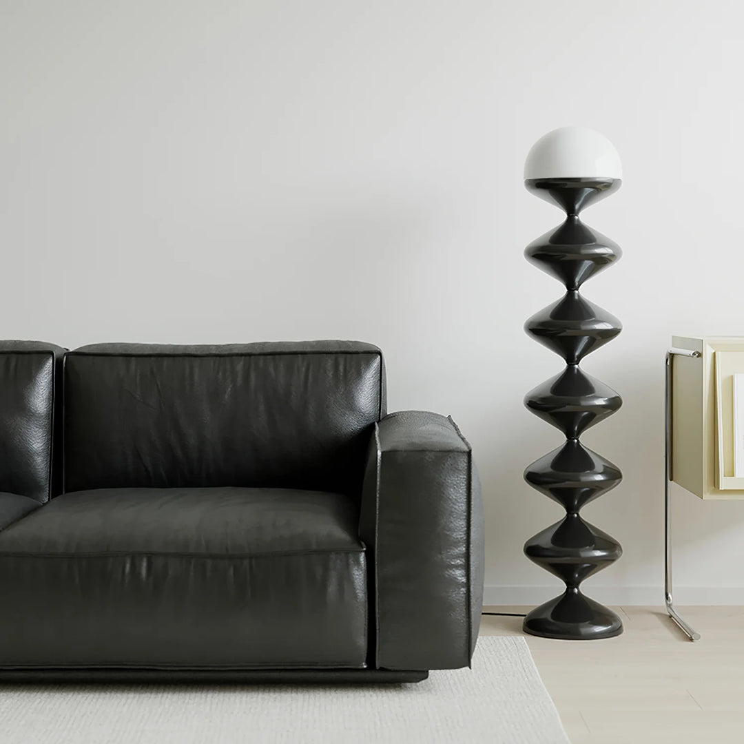 Minimalist home decor featuring a sleek Gourd Lamp with a spiral black base and a clean white top, placed next to a black leather sofa. The simple yet striking design complements the neutral, light-filled room, emphasizing a modern and understated elegance.