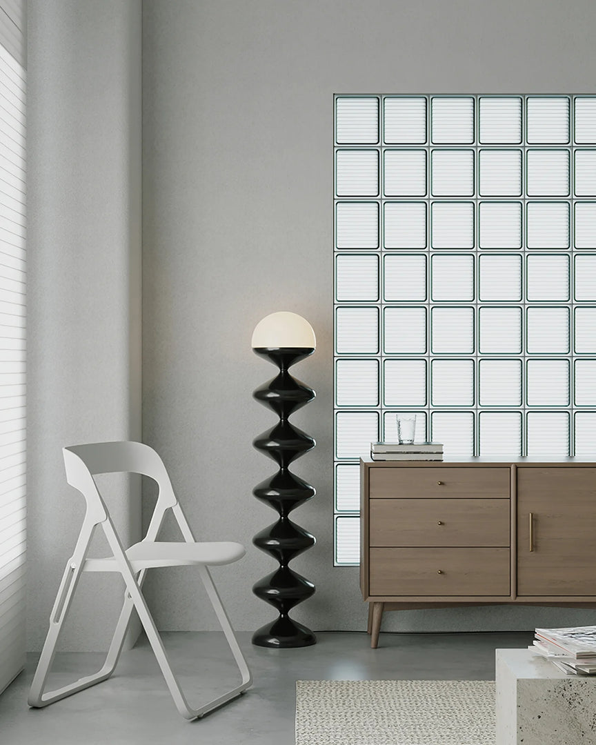 Sleek and contemporary interior featuring a Modern Geometric Gourd Lamp with a spiraled black base and white top, placed next to a stylish white folding chair. The backdrop includes a geometric patterned wall and a minimalist wooden cabinet, emphasizing the lamp's role in a clean and modern space design.