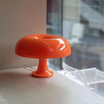 Load image into Gallery viewer, Vibrant orange Mushroom Playful Table Lamp with a sleek, glossy finish, perfectly positioned on a modern table near a window, adding a pop of color and a playful touch to the contemporary interior design.
