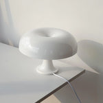 Load image into Gallery viewer, The soft cream Mushroom Playful Table Lamp bathes in the gentle morning light, its polished surface reflecting the serene surroundings of a minimalist interior, creating a peaceful and inviting atmosphere perfect for relaxation or reading.
