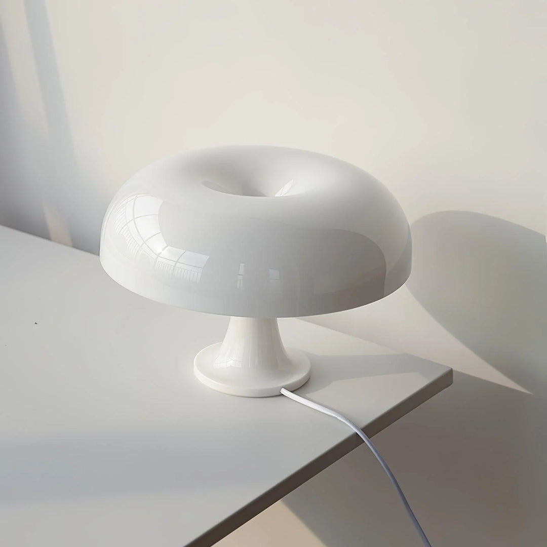 The soft cream Mushroom Playful Table Lamp bathes in the gentle morning light, its polished surface reflecting the serene surroundings of a minimalist interior, creating a peaceful and inviting atmosphere perfect for relaxation or reading.