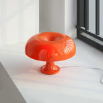 Load image into Gallery viewer, A vibrant orange Mushroom Playful Table Lamp elegantly captures morning light beside a window, its glossy finish and curvaceous design reflecting the serene surroundings in a modern and stylish interior.
