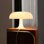 Load image into Gallery viewer, A soft cream Mushroom Playful Table Lamp casts a warm, inviting glow atop a classic wooden cabinet, the gentle illumination complementing the tranquil ambiance of a dimly lit room with flowing sheer curtains.
